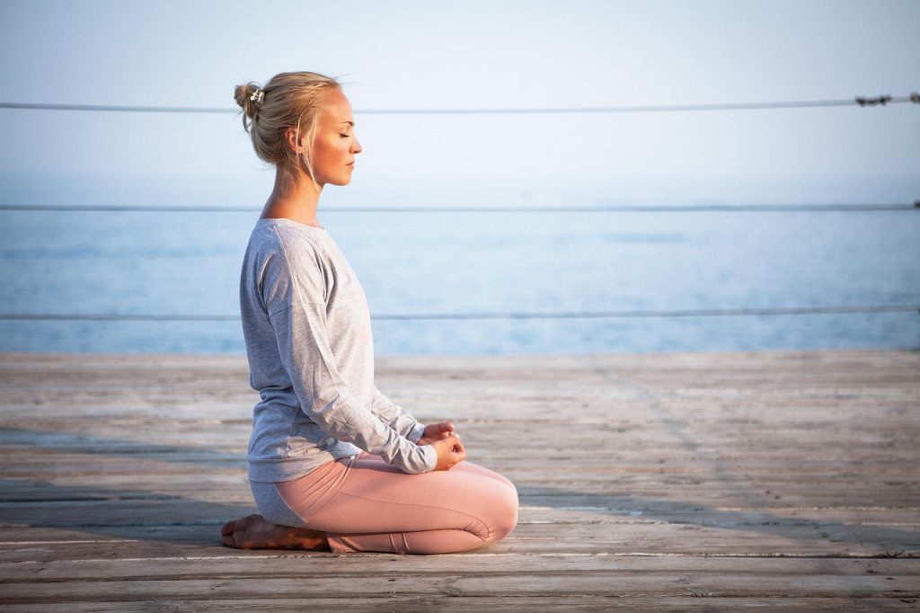 Mujer meditando frente al mar, practicando pausa consciente y autocuidado emocional, reconexión interior y bienestar