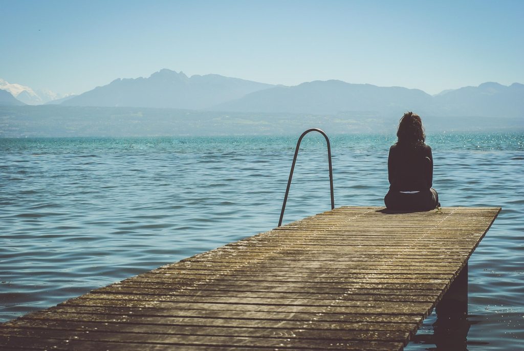 Mujer sentada sola en muelle, mirando el lago, simbolizando introspección y sostenerse emocionalmente
