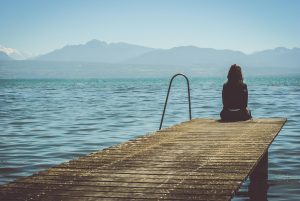 Mujer sentada sola en muelle, mirando el lago, simbolizando introspección y sostenerse emocionalmente