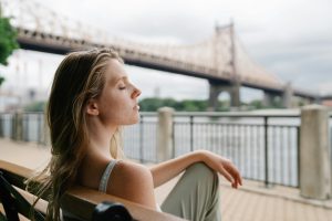 Mujer joven en pausa consciente frente a puente urbano, simbolizando descanso emocional y autocuidado