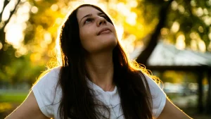 Mujer con cabello largo mirando hacia la luz dorada en la naturaleza, representando serenidad y autoliderazgo emocional