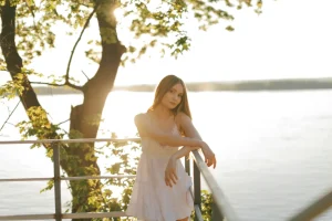 Mujer apoyada en una barandilla al atardecer, mirada serena junto al agua: calma y enfoque para sostener metas en 2026.