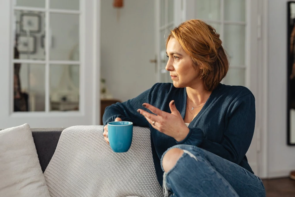 Mujer pensativa en casa sosteniendo una taza mientras reflexiona sobre su autoexigencia y voz crítica
