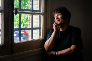 Mujer madura reflexionando junto a una ventana sobre su voz interior crítica y diálogo interno