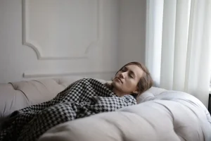 Mujer agotada descansando plácidamente en el sofá tapada con una manta, dándose permiso para sentir su cansancio.